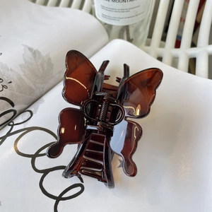 Detailed view of amber butterfly hair claw clip with glossy finish on a white magazine