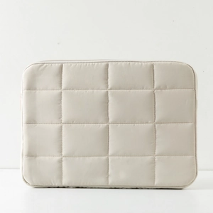 Close-up of quilted cream laptop sleeve featuring classic square stitching and top zipper
