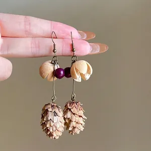 Detail view of ethnic style drop earrings with pine cone and purple bead elements