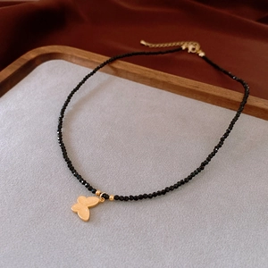 Close-up of black faceted beads necklace with a golden butterfly charm on a velvet tray
