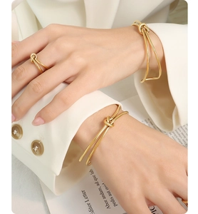 Detail of 18k gold plated knot bracelets and matching ring on model with white blazer