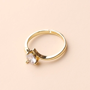 Detail of adjustable gold ring with a sparkling clear round gemstone on pink background