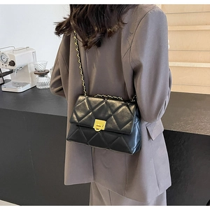 Quilted black chain bag worn over a grey blazer, showing the gold hardware lock and strap