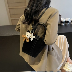 Schwarze Beuteltasche mit Bärenanhänger, präsentiert an einem schicken Modell-Outfit