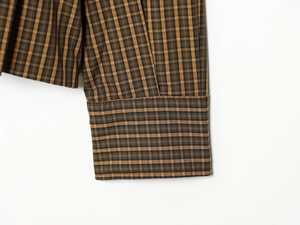 Detail of brown plaid shirt sleeve cuff showing precise stitching and buttonhole texture