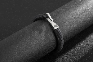 Close-up of black braided leather bracelet featuring a polished silver stainless steel hook clasp