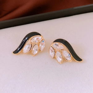 Detail view of gold earrings with black enamel and marquise crystals in wing design