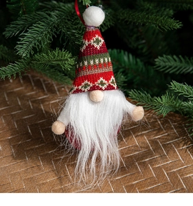 Close-up of festive Christmas gnome ornament with knitted hat hanging on a tree branch