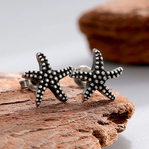 Vintage silver starfish stud earrings with textured detail on a rustic wood background