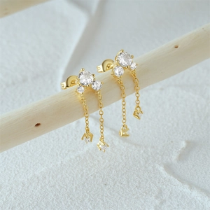 Detail of gold tassel earrings with clear zircons hanging on a white branch backdrop