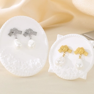 Detail view of gold and silver bow-knot stud earrings with freshwater pearls on silk