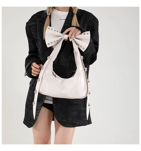 Close-up of a cream patent leather shoulder bag with a large bow and silver stud details