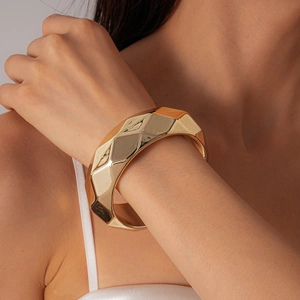 Macro shot of a thick golden geometric faceted metal bangle on a model's wrist