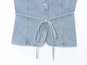 Gros plan du gilet en jean bleu clair avec boutons métalliques et taille coulissante