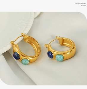Detailed view of C-shaped gold hoop earrings with inset blue and turquoise gemstones