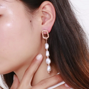 Gros plan de boucles d'oreilles géométriques or rose avec perles baroques blanches