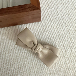 Détail d'une pince à cheveux nœud en cuir PU beige sur fond en maille texturée