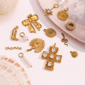 Detail of vintage 18K gold bow, cross, and pearl charms arranged on a textured shell