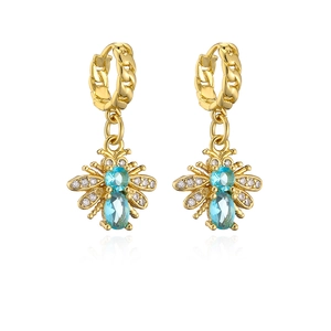 Detailed view of gold earrings with blue stones and zircon wings on white background