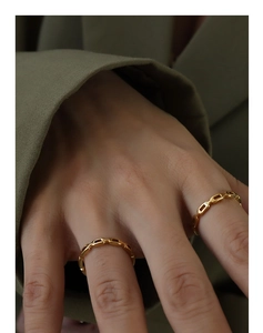 Detailed close-up of golden chain link rings worn on model fingers with green suit background