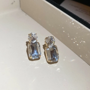 Macro detail of gold earrings featuring vertical round and rectangular clear crystals