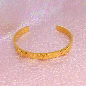 Gros plan d'un bracelet ouvert doré orné de motifs d'abeilles en 3D sur fond texturé