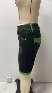 Detailansicht der schwarzen Denim-Shorts mit grünen Kontrastnähten und Distressed-Rissen