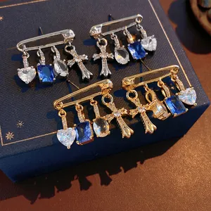 Silver safety pin earrings with cross heart zircon charms on a luxury jewelry box