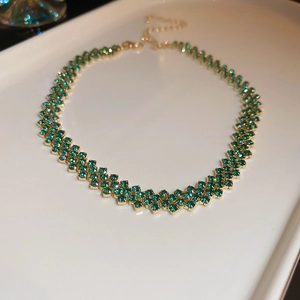 Dettaglio di una collana girocollo dorata con strass verde smeraldo e chiusura regolabile