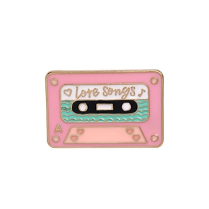 Macro detail of pink enamel cassette tape brooch with gold metal and Love Songs text