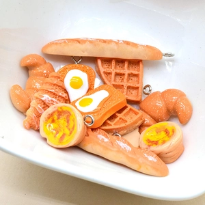 Miniature resin food charms including croissants and toast in a white bowl