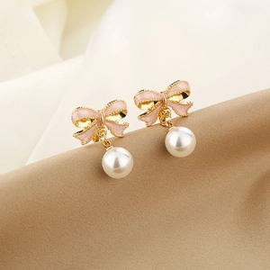 Detailed macro view of pink enamel bow earrings with round white pearl drop on silk
