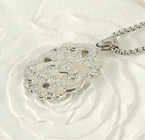 Macro side view of silver dragon pendant with box chain on floral background