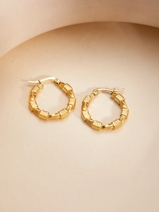 Close-up of golden twist hoop earrings with ribbed texture and latch clasp closure