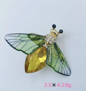 Detailed close-up of a bee brooch with green wings and yellow gemstone on a white base