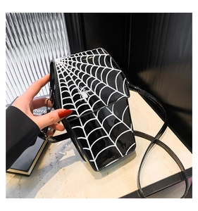 Detail of glossy black patent leather crossbody bag featuring a white spider web pattern