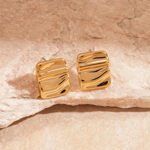 Macro detail of gold wavy square studs on natural textured stone background with sharp focus
