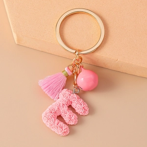 Close-up of pink letter E keychain featuring rose patterns with tassel and bell charms