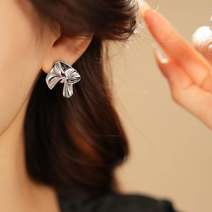 Close-up of minimalist silver irregular metal earring worn by a model in soft lighting