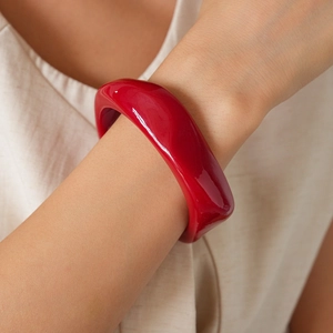 Close-up of wide red acrylic geometric bangle bracelet worn by model on neutral background