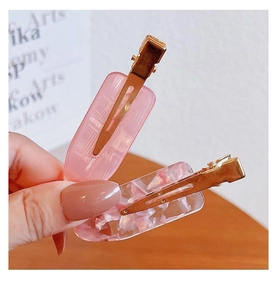 Close-up of two pink acrylic seamless hair clips with gold metal base and petal texture