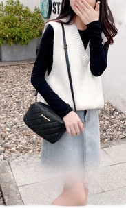 Fashionable black quilted crossbody bag with gold hardware shown on a casual female model
