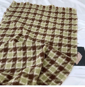 Detail of soft brown and green houndstooth scarf with fine tassels on white bedding