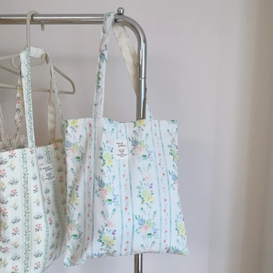 Dettaglio di borse tote in cotone a fiori blu con etichette appese a un supporto