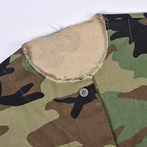 Detail of camouflage vest collar showing a gray button and raw hem on twill fabric