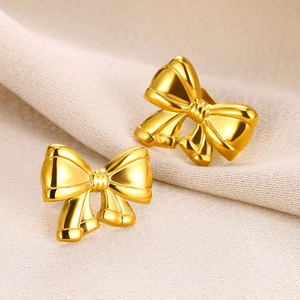 Detailed macro view of 18K gold-plated bow-knot stud earrings on white textured fabric