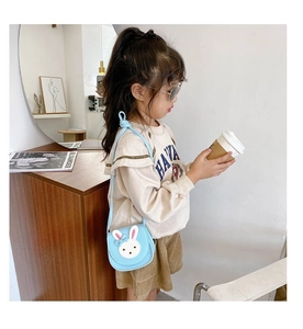 Light blue rabbit shaped mini shoulder bag for kids shown on a young model in a cozy room