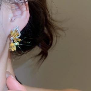 Detail shot of elegant butterfly zircon earrings in amber yellow on a model ear