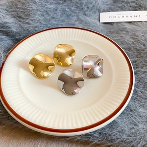 Macro shot of irregular polished gold and silver plated metal earrings on a ceramic dish