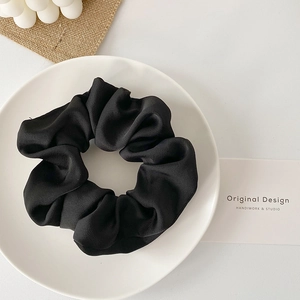 Close-up detail of smooth black satin scrunchie with elegant silk texture on white plate